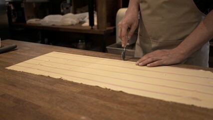 Male hands cutting dough rolled on big wooden table at the restaurant kitchen. Making ravioli, cutting big long slice of raw dough, italian cuisine