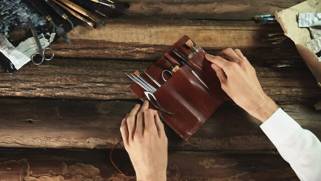 Male painter opens leather case with tools, brushes, Palette knife