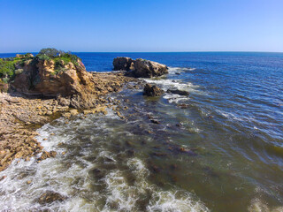 gorgeous aerial shot of the waves and the deep blue ocean water and the large rocks on the beach...