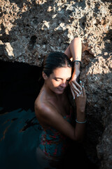 Young woman in sea water, resting on top of a rock, while the sunlight hits her face
