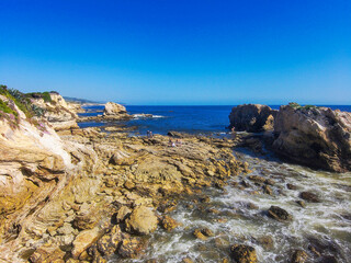 majestic aerial shot of the deep blue ocean water, large rock formations and beach with blue sky at...