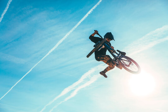 Carefree man jumping while performing stunt with bicycle against blue sky during sunset
