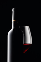 Bottle and glass of red wine on a black background.