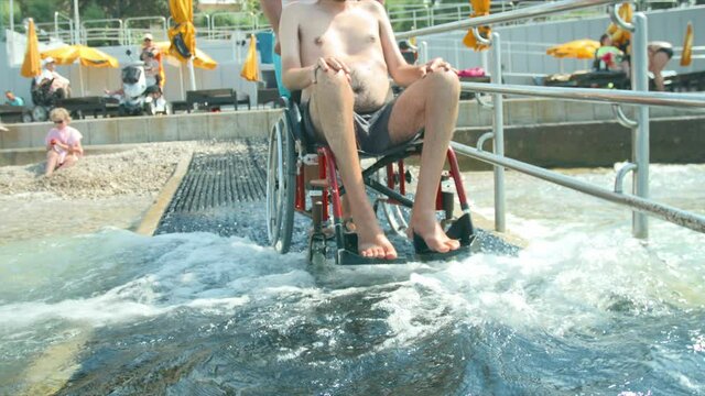 Disabled man at beach going for a swim with help of a wheelchair and assistant.