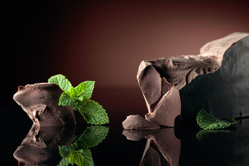 Large piece of dark bitter chocolate with mint on a black reflective background.