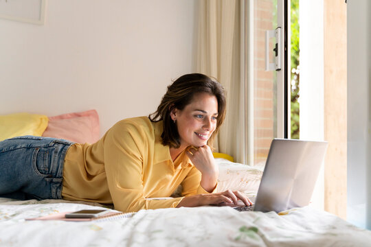 Smiling woman using laptop in bedroom