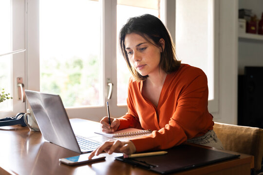 Businesswoman using smart phone while working at home - Powered by Adobe