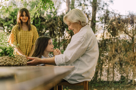 Woman looking at senior woman playing with cute granddaughter in yard