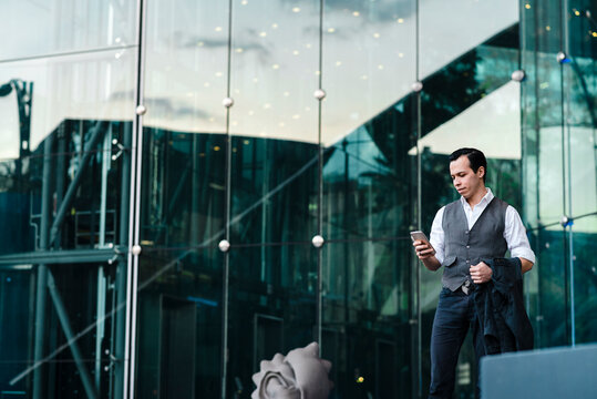 Businessman Using Smart Phone While Standing Outside Office Building In City