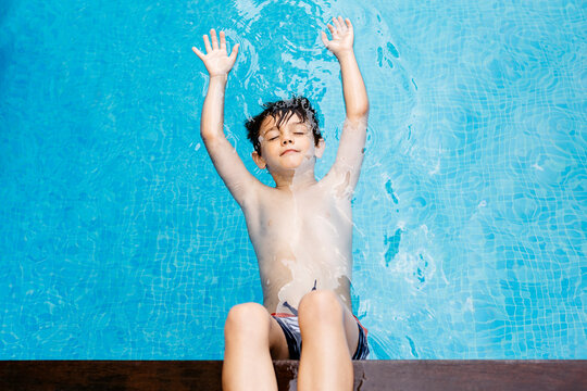 Boy floating in pool with legs support at poolside