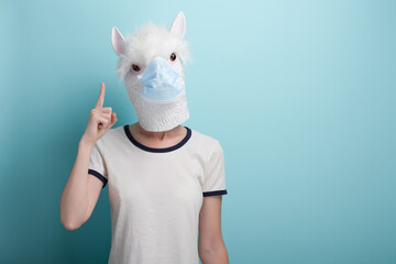 Young woman wearing alpaca and protection medical mask pointing up with index finger, capture the...