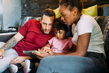 Parents with daughter using digital tablet while relaxing on sofa at home
