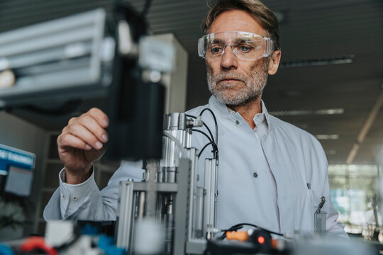 Male scientist with protective eyewear examining machine in laboratory