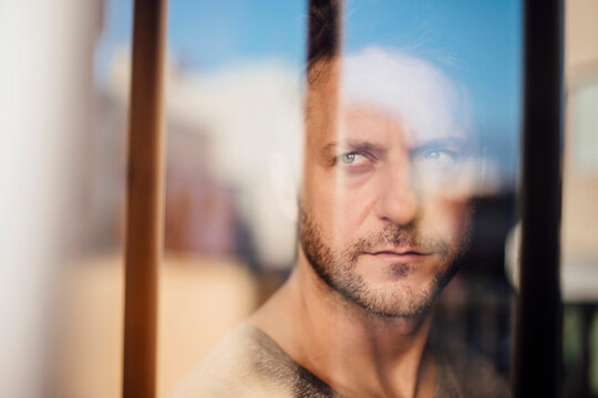 Close-up of thoughtful man looking through window seen through glass