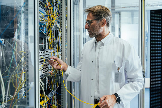 Mature man plugging transceiver on fiber optic cable into rack