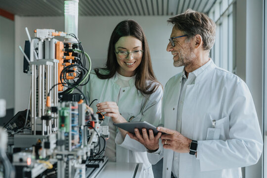 Mature man showing digital tablet to female colleague while standing by machinery in laboratory