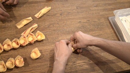 Cook preparing tortellini, rolling on wooden kitchen table, top view shot. Male hands cooking italian food, handmade tortellini at the restaurant kitchen