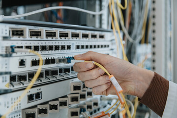 Close-up of woman plugging fiber optic cable in equipment at data center