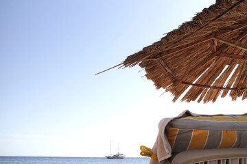 beach umbrella on a sand at the shore near the sea and ship on the horizon under blue sky laying...