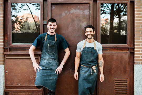 Smiling Bakers In Apron Standing Against Door