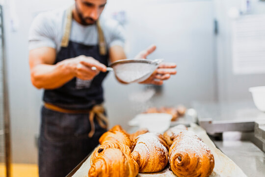 Baker spraying powdered sugar on croissants at bakery