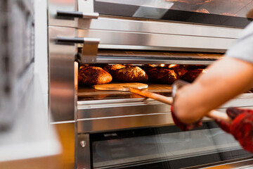 Cropped hand of male baker baking bread in oven at bakery