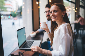 Smiling woman using laptop and drinking coffee in cafe