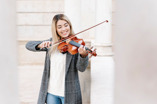 Blond young woman playing violin in city