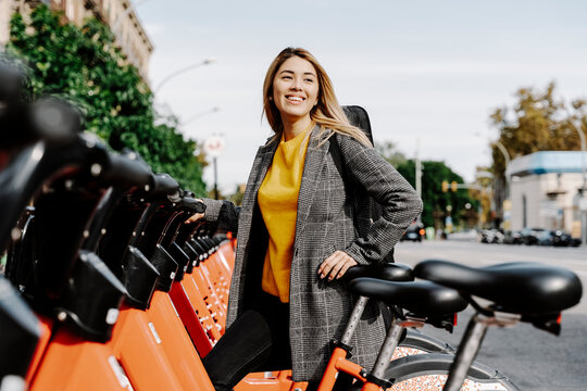Young woman with violin case renting bicycle in city