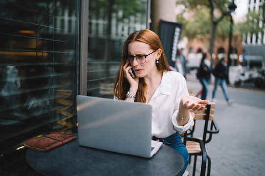 Irritated businesswoman speaking on cellphone in outdoor cafe