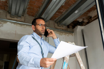 Architect with plan on the phone in a house under construction