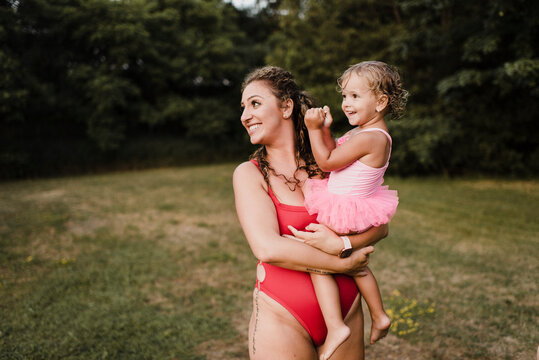 Happy mother in swimsuit carrying little daughter on a meadow
