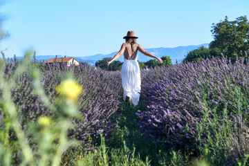 Woman wearing white dress and hat walking amidst lavender field against clear sky