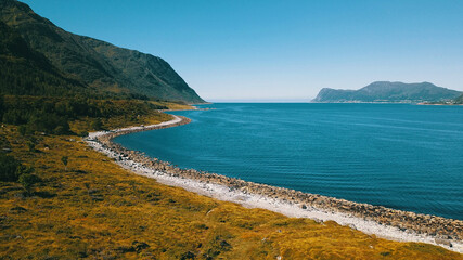 Coastline with mountains. Grassy slope and emerald water.