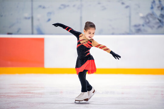 Little girl ice skater in beautiful black red dress ice skating of an indoor ice arena.