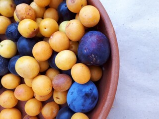 Yellow and blue plums in a ceramic Cup close - up on a light background.