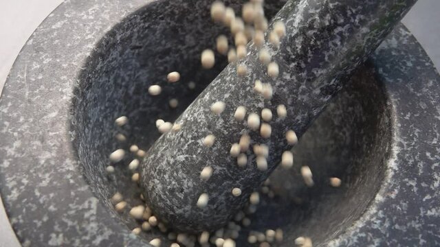 Spicy white peppercorns are falling into the grey stone mortar in slow motion