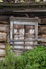 The old window of an abandoned log house with closed shutters is clogged with boards.