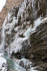 Fototapeta na wymiar Vertical image of winter river and rozen icicles of big waterfall. Scenery winter landscape.