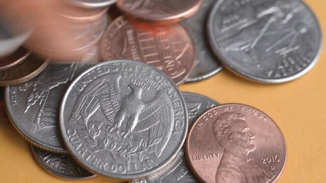 Spare change falling onto a matte surface.  Close up macro view of American coins piling up.  Quarters, dimes, nickels, and pennies all slide into frame.  Demonstrates currency, moving money, saving. 