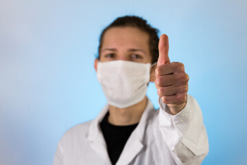 An adult male dressed in a white lab coat with a protective face mask on while giving a thumbs up. Ready to work in a clean room or laboratory
