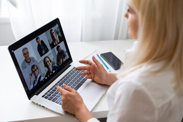 Fototapeta na wymiar Back view of business woman talking to her colleagues about plan in video conference. Multiethnic business team using laptop for a online meeting in video call. Group of people smart working from home