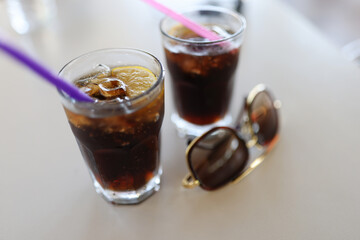 Two full straw glasses and sunglasses stand on white table. Cocktail, lemon wedges and ice are poured in glass.