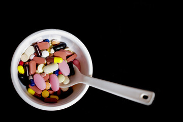 bowl of medicine pills tablets capsules in black background