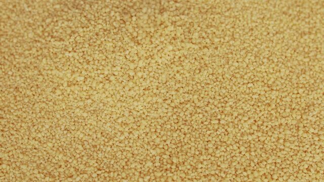 Raw organic couscous grains fall and crumble. Couscous background. Selective focus.