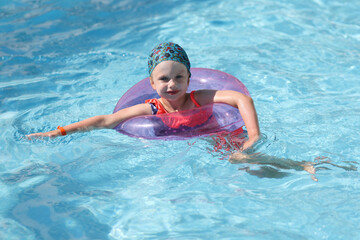 Fototapeta na wymiar Beautiful girl swim in blue pool with inflatable ring. Professional swimming training for children.