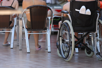 Disabled boy sit in wheelchair and look. People sit in row on chairs.