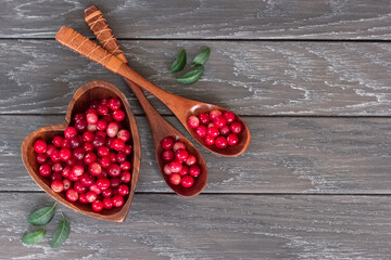 ripe cranberries in a wooden bowl and spoons top view. cranberries on a wooden background. copy of the space. the cranberries lay flat