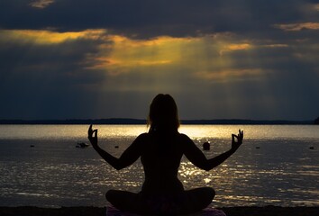 silhouette of a young woman practicing yoga on the beach at the sunset