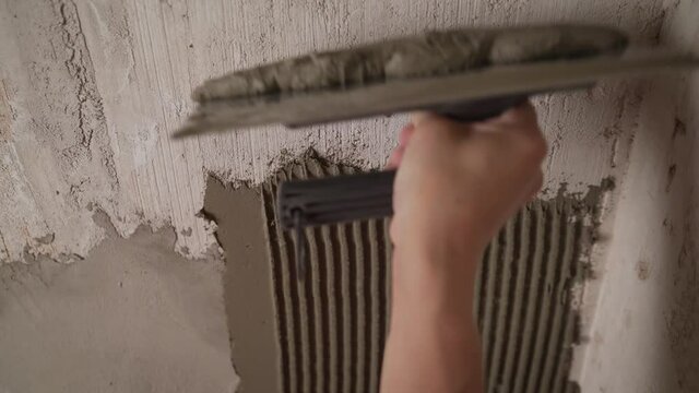 A worker applies an adhesive solution to a tile wall. A professional designer applies glue before laying ceramic tiles on the wall